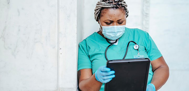 Doctor in scrubs and mask looks at a tablet.