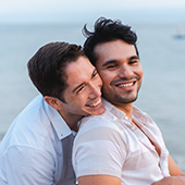two men hugging on the beach looking away from camera