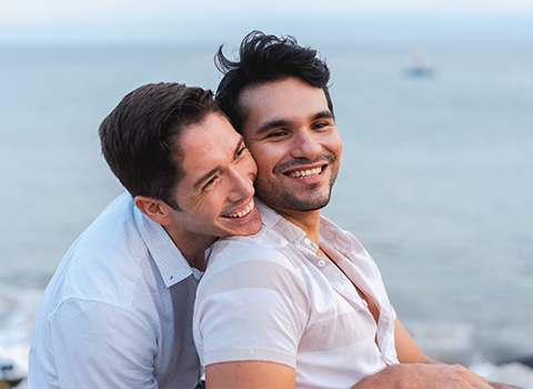 two men hugging on a beach, looking beyond the camera