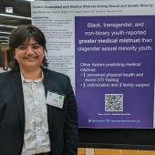 Afiya Sajwani wearing a suit and smiling in front of their award-winning poster